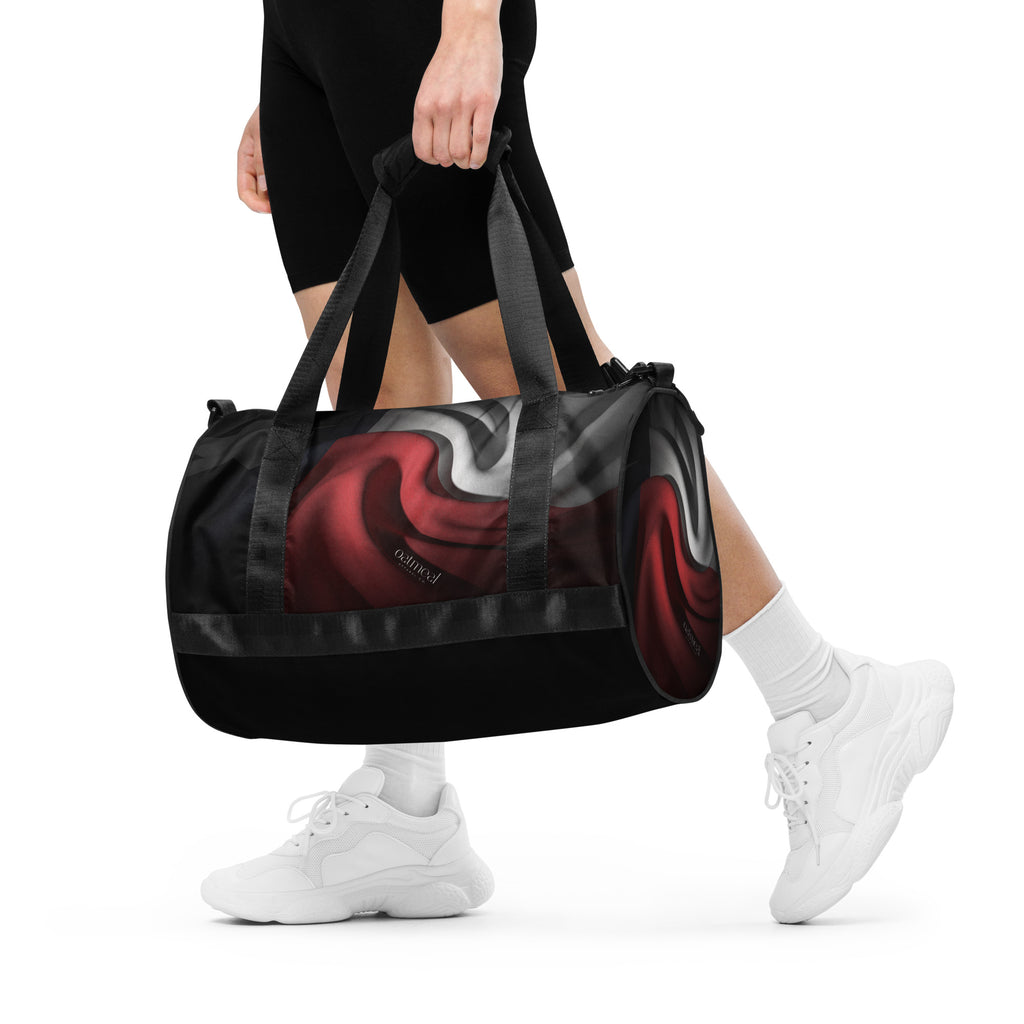 Person holding a black duffel bag with red and white custom design at Oatmeal Apparel Co.