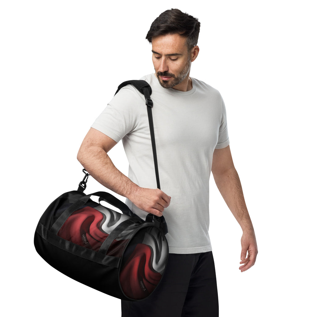 Man holding a black duffel bag with red and gray design on a white background at Oatmeal Apparel Co.