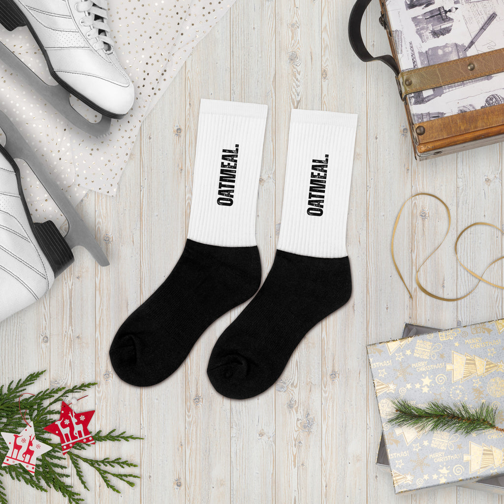 Black socks with 'OATMEAL' branding on a wooden surface with holiday decor at Oatmeal Apparel Co.