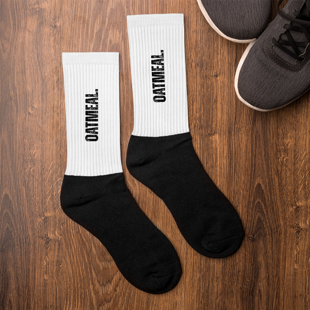 Black and white socks with 'OATMEAL.' branding on a wooden surface at Oatmeal Apparel Co.