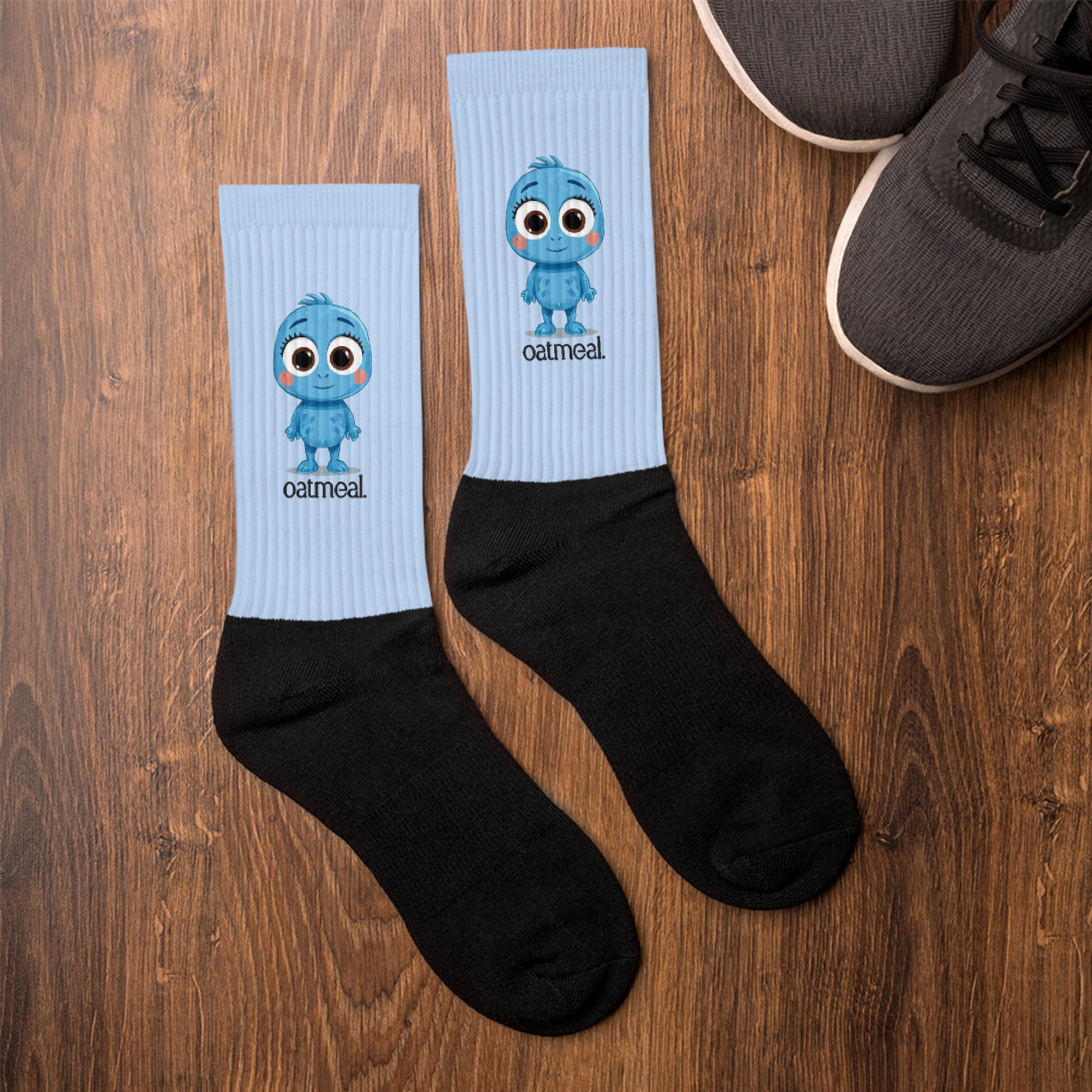 Two pairs of socks with Oatmeal cartoon character design on a wooden surface at Oatmeal Apparel Co.