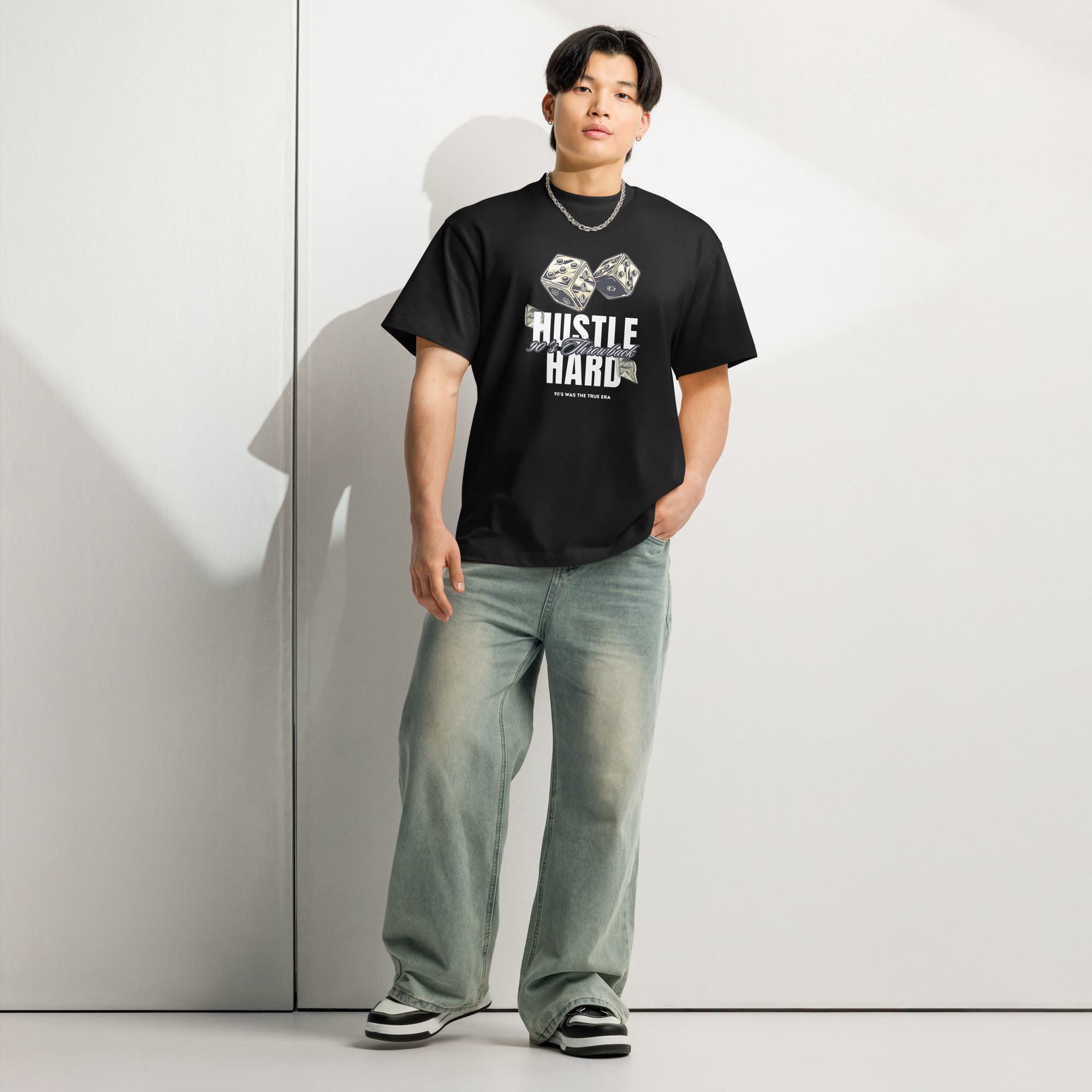 Person wearing a black t-shirt with 'Hustle Hard' text and graphic, standing against a light gray wall at Oatmeal Apparel Co.