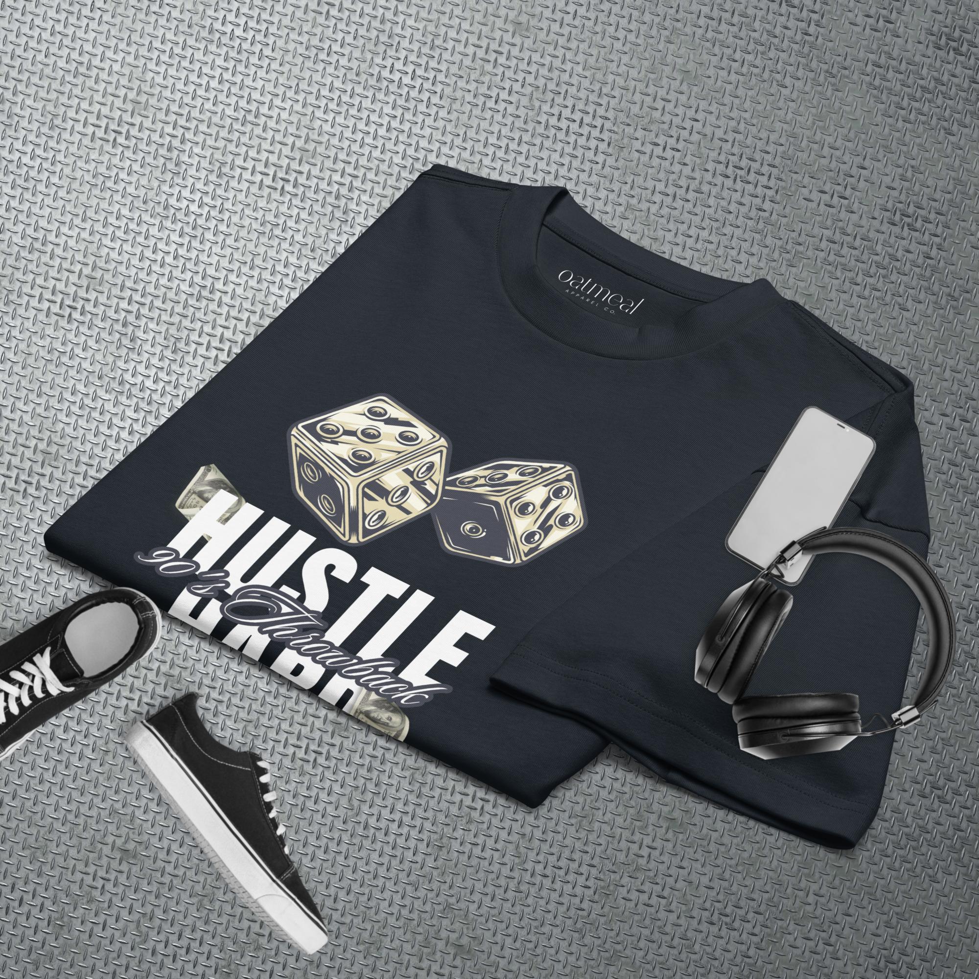 Black t-shirt with dice design and text, placed on a textured gray surface with sneakers and headphones at Oatmeal Apparel Co.