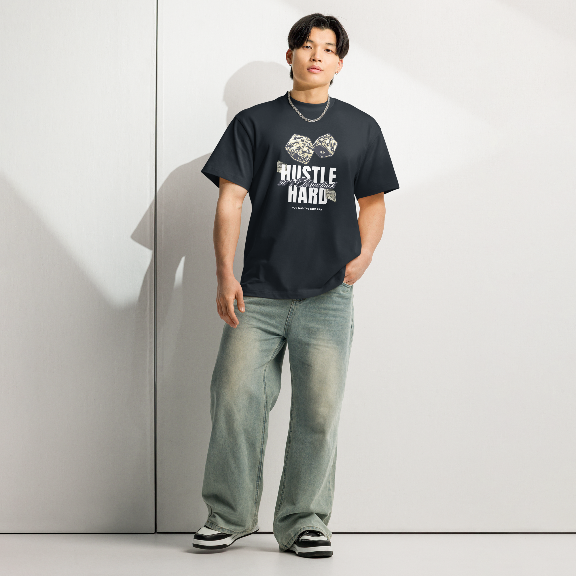 Person wearing a black t-shirt with 'HUSTLE HARD' text and graphic, standing against a light gray wall at Oatmeal Apparel Co.