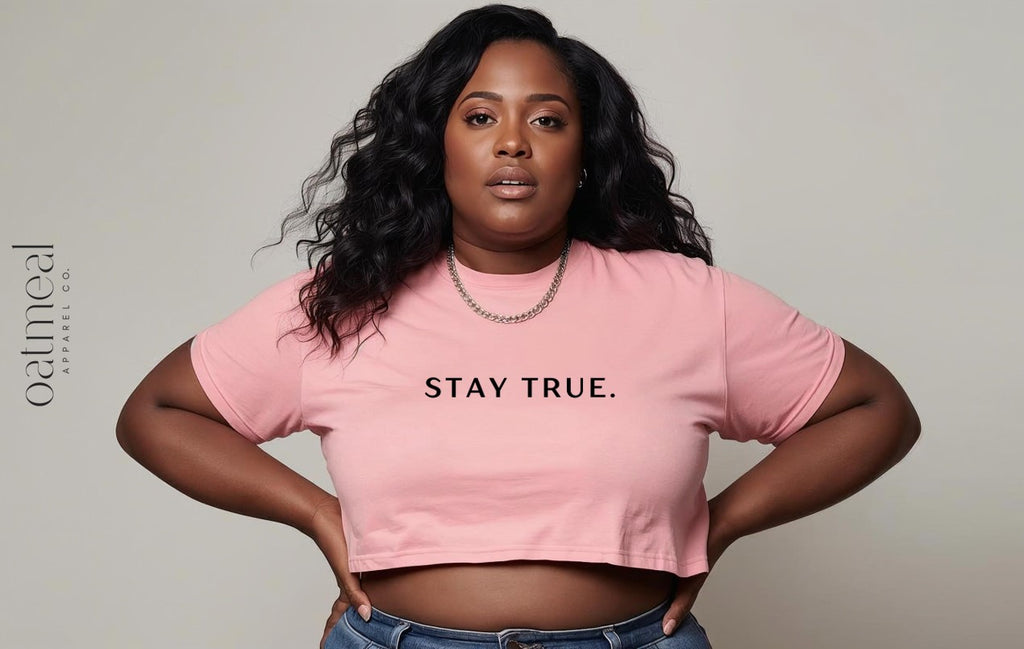 Person wearing a pink crop top with 'STAY TRUE.' text on a plain background from Oatmeal Apparel Co.