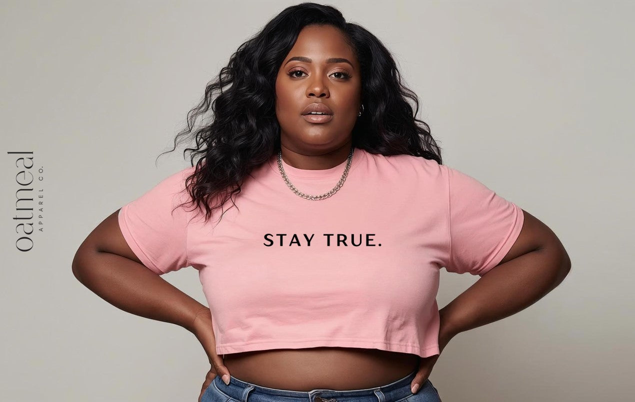 Person wearing a pink crop top with 'STAY TRUE.' text on a plain background from Oatmeal Apparel Co.