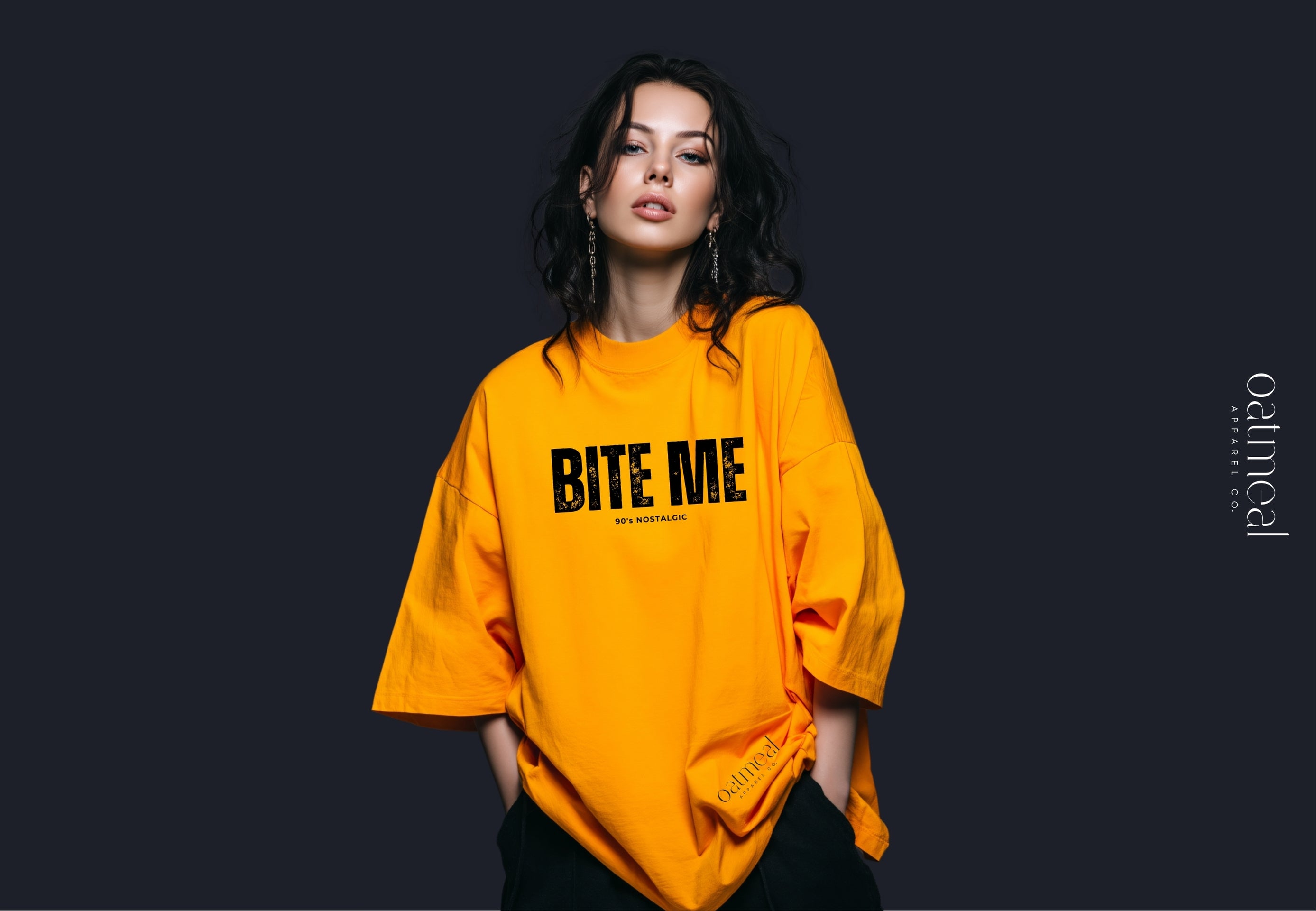 Person wearing a bright orange oversized t-shirt with 'BITE ME' text on a dark background at Oatmeal Apparel Co.