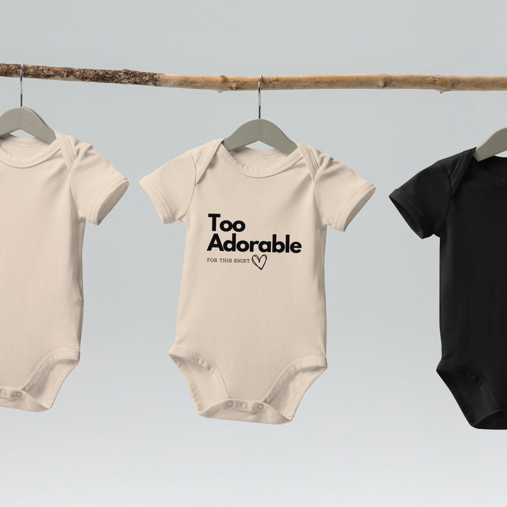 Three baby onesies hanging on a rack with text on one of them at Oatmeal Apparel Co.