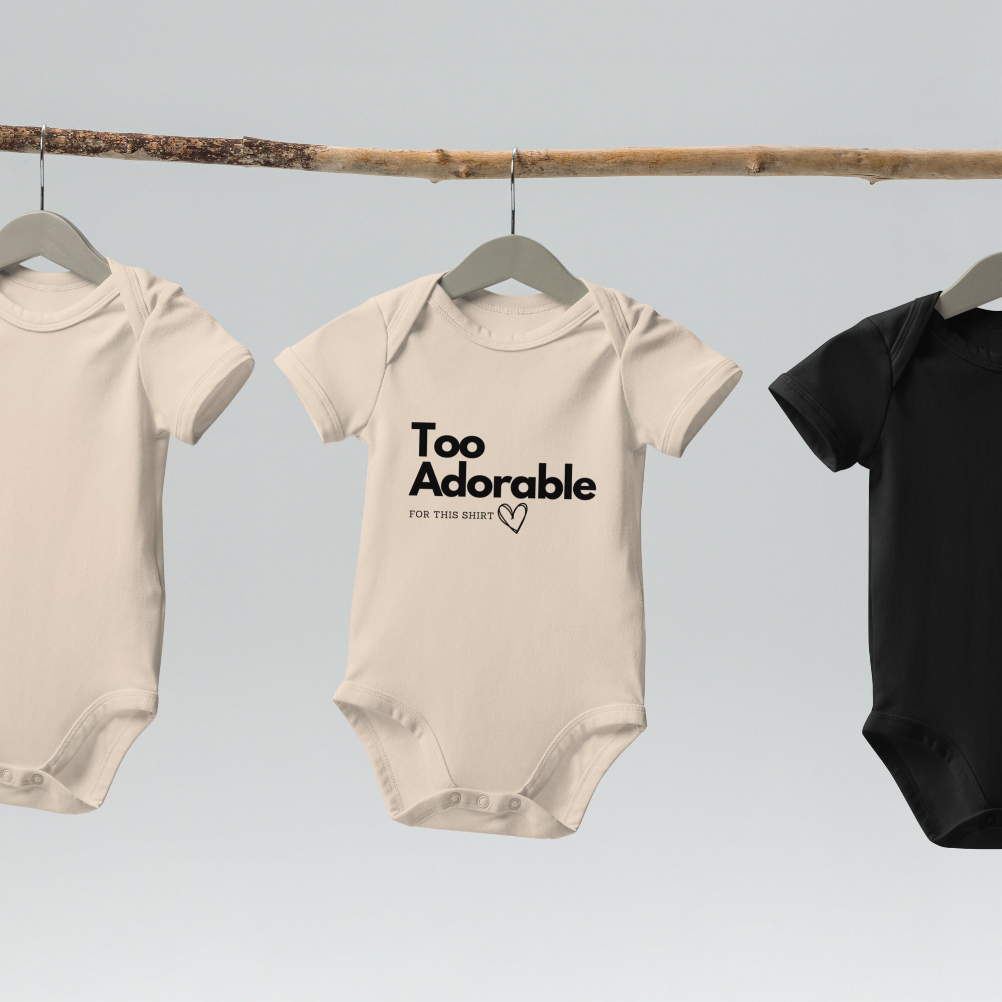 Three baby onesies hanging on a rack with text on one of them at Oatmeal Apparel Co.