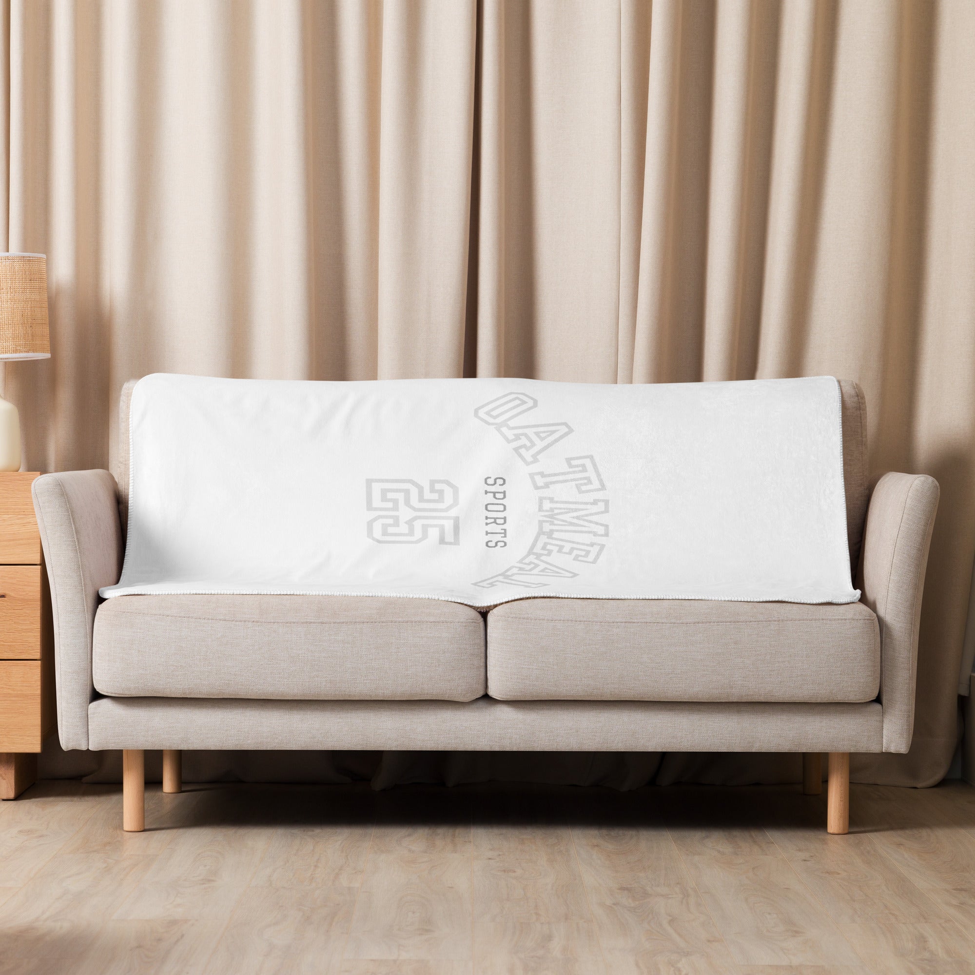 Beige sofa with a white Oatmeal Sports No.25 throw blanket draped over it against beige curtains at Oatmeal Apparel Co.