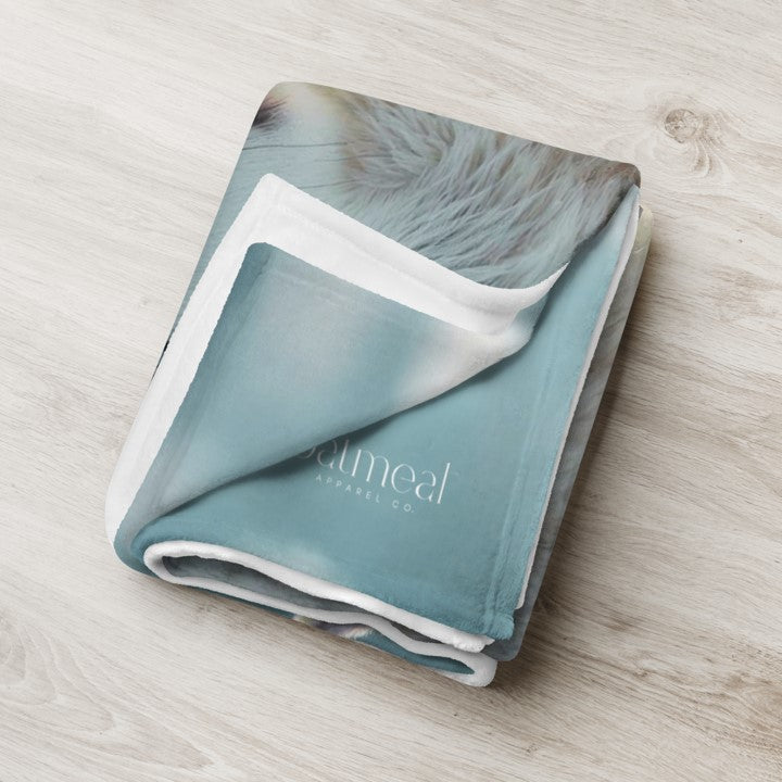 Folded Wolfdog blanket with white trim on a light wooden surface with 'oatmeal' branding at Oatmeal Apparel Co.