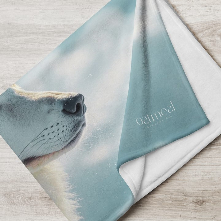 Teal blanket with wolfdog face design and 'oatmeal' branding on a wooden surface at Oatmeal Apparel Co.
