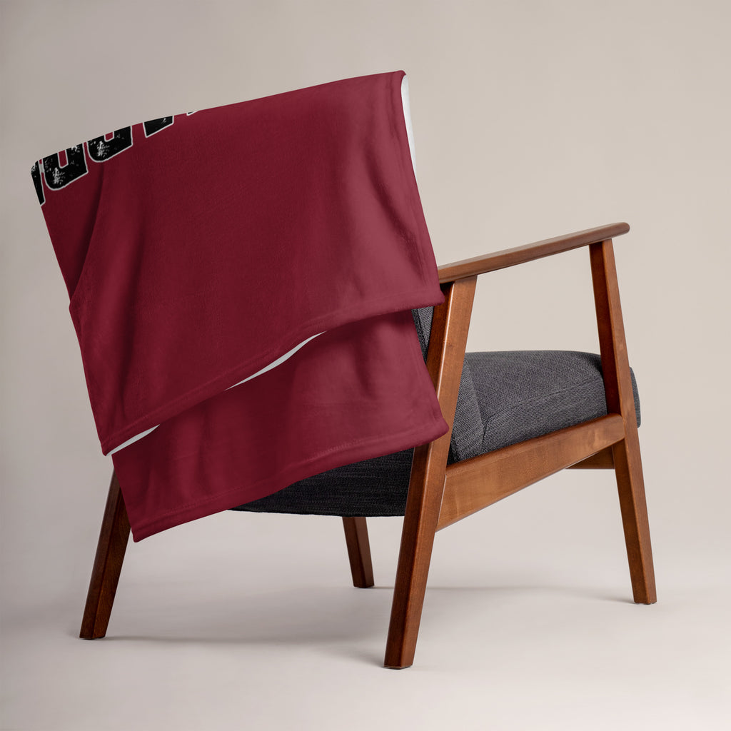 Wooden armchair with a gray cushion and a red blanket draped over it on a beige background at Oatmeal Apparel Co.