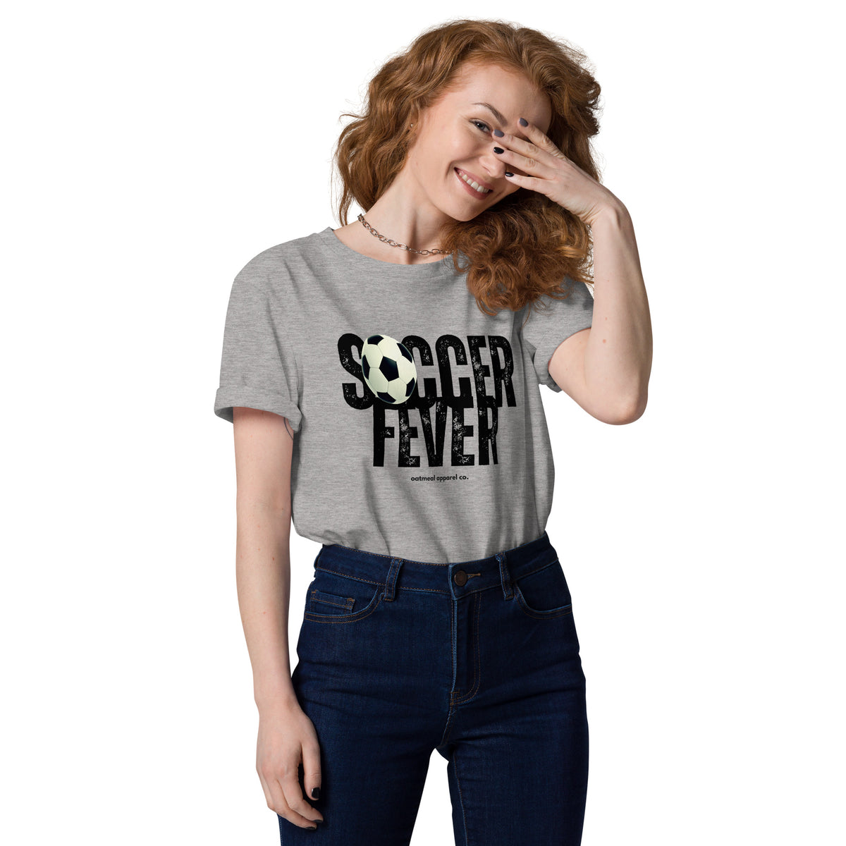 A woman with red hair wearing a heather gray graphic t-shirt that says 'SOCCER FEVER' in black with a soccer ball graphic, paired with dark blue jeans at Oatmeal Apparel Co.