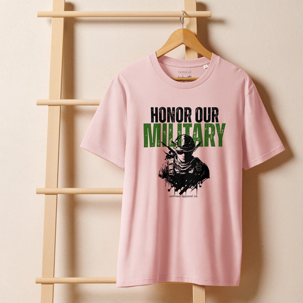 Pink t-shirt with 'Honor Our Military' text and graphic on a wooden hanger against a beige wall available at Oatmeal Apparel Co.