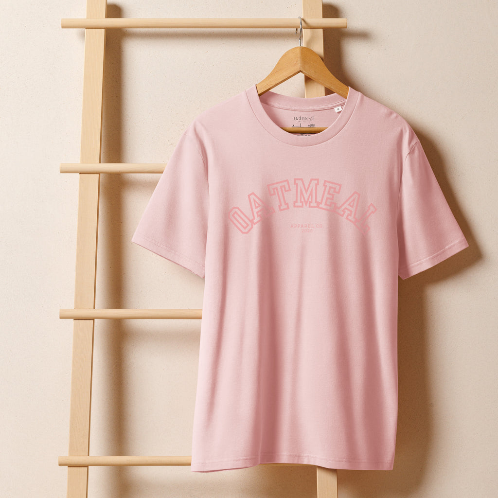 Pink t-shirt with 'OATMEAL' branding on a wooden hanger against a beige wall at Oatmeal Apparel Co., Sports Edition Design.