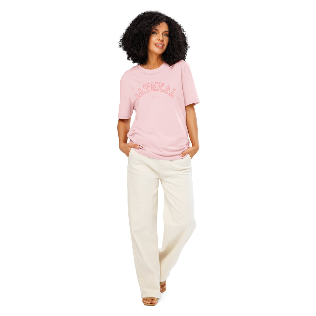 Woman wearing a pink t-shirt with 'OATMEAL APPAREL CO.' design and white pants on a white background at Oatmeal Apparel Co., Sports Edition Design.