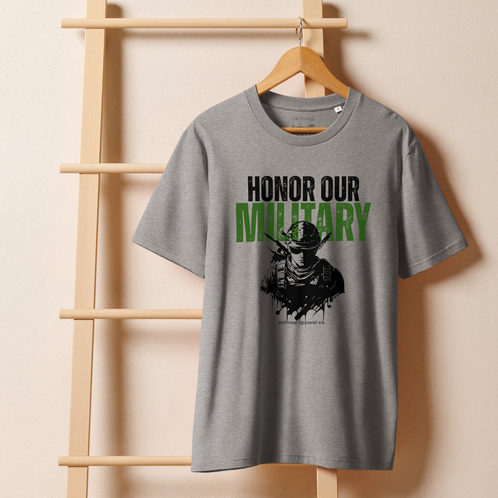 Gray t-shirt with 'Honor Our Military' graphic on a wooden hanger against a beige wall avail at Oatmeal Apparel Co.