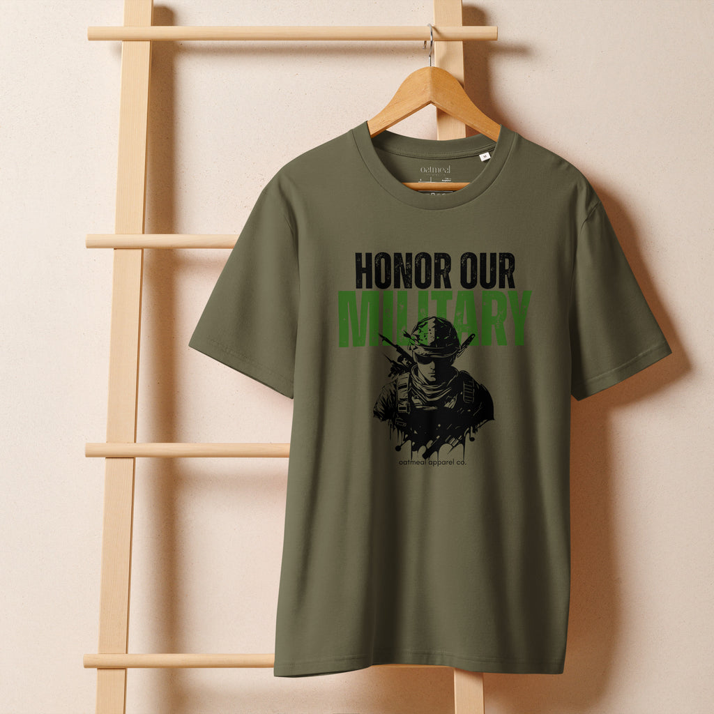 Green t-shirt with 'Honor Our Military' text on a wooden hanger against a beige wall avail at Oatmeal Apparel Co.