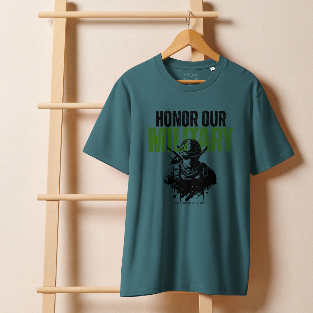 Teal t-shirt with 'Honor Our Military' text on a wooden hanger against a beige wall at Oatmeal Apparel Co.
