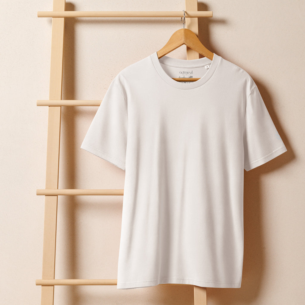White Woven Secrets™ t-shirt on a wooden hanger against a beige wall at Oatmeal Apparel Co.