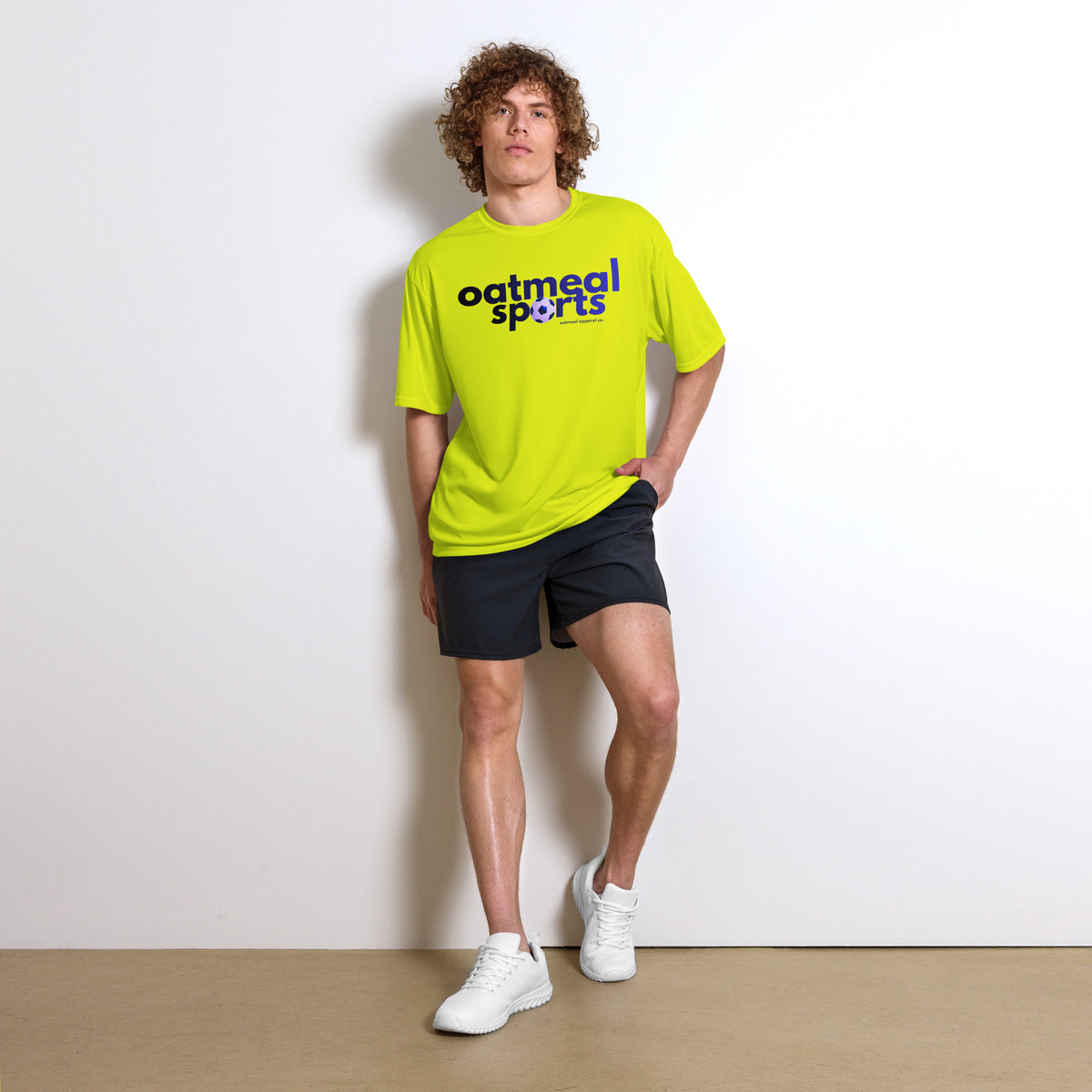 Person wearing a bright yellow t-shirt with Oatmeal Sports from Oatmeal Apparel Co., black shorts, and white sneakers against a plain background