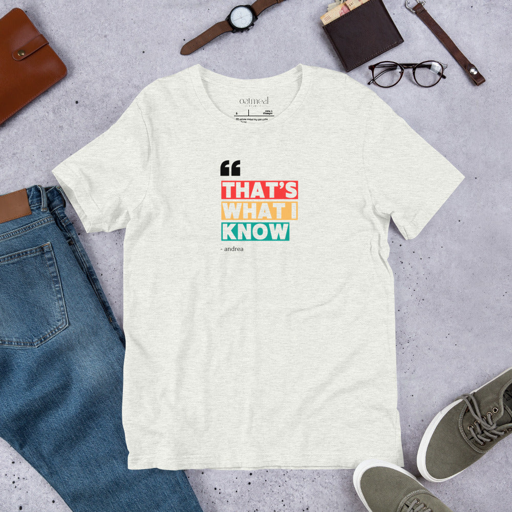 White t-shirt with colorful text design and 'oatmeal' branding on label, with a gray surface with jeans, shoes, and accessories at Oatmeal Apparel Co.