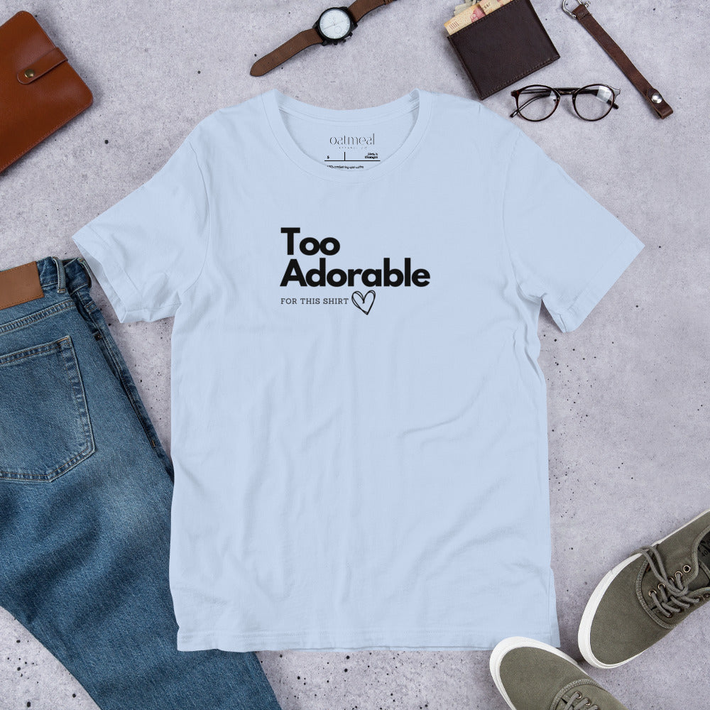 Light blue t-shirt with 'Too Adorable' text on a concrete surface with jeans, shoes, and accessories available at Oatmeal Apparel Co.