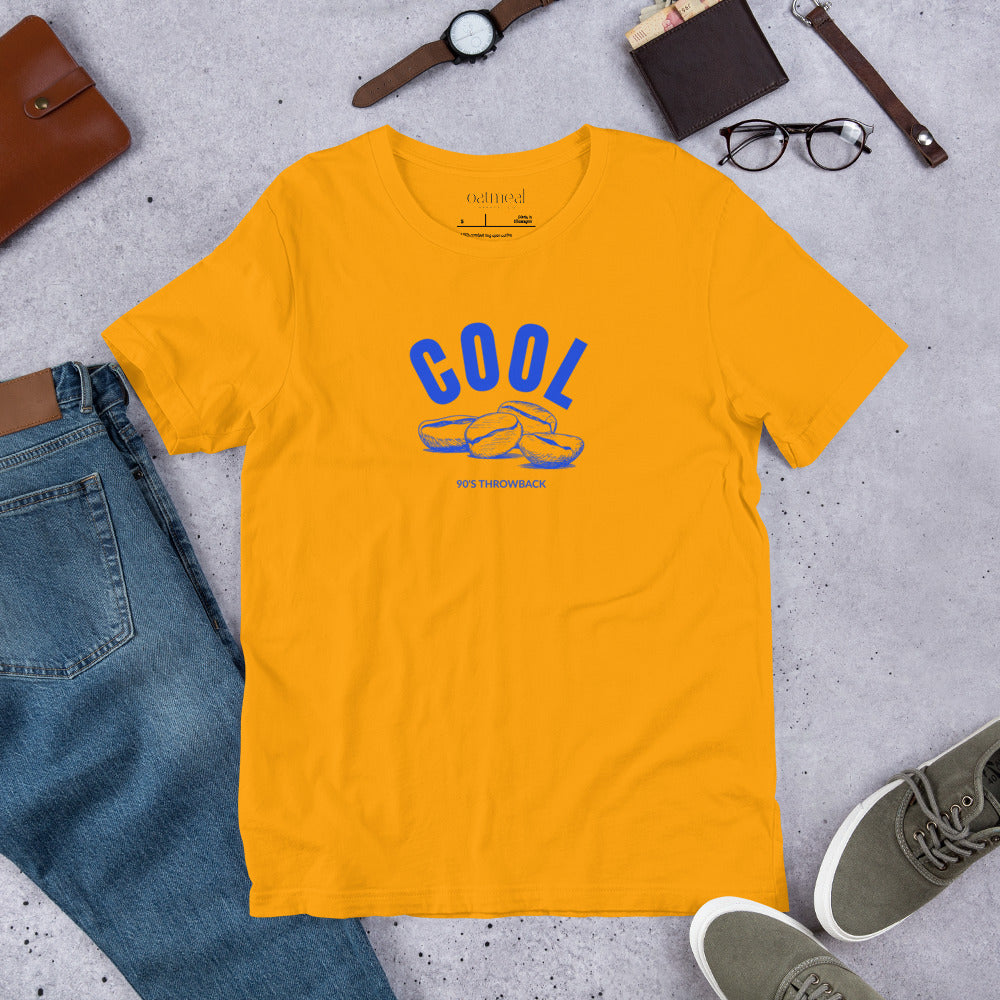 Gold t-shirt with 'COOL Beans' graphic on a gray surface with jeans, shoes, and accessories at Oatmeal Apparel Co.