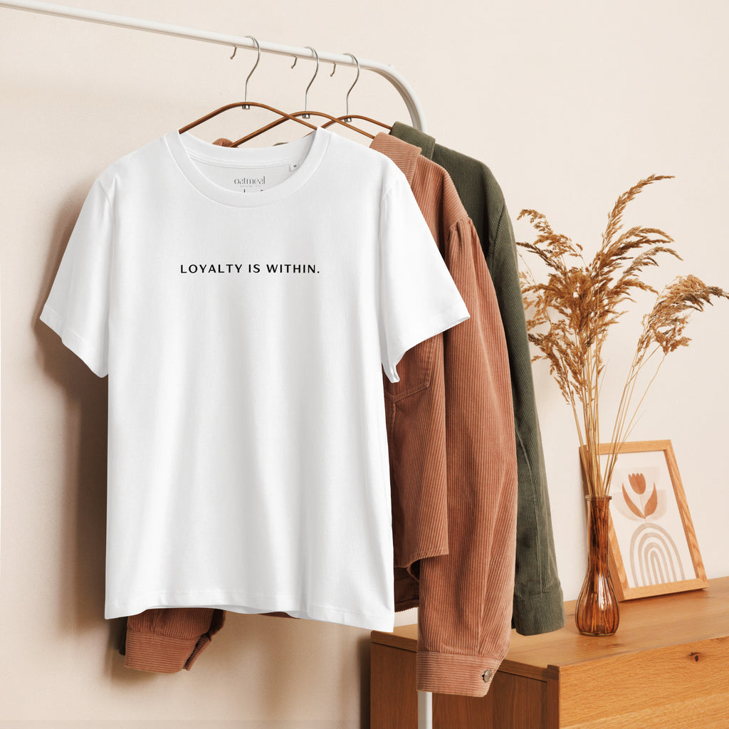 Women's Organic White t-shirt with 'LOYALTY IS WITHIN' text on a rack with other clothing items at Oatmeal Apparel Co.